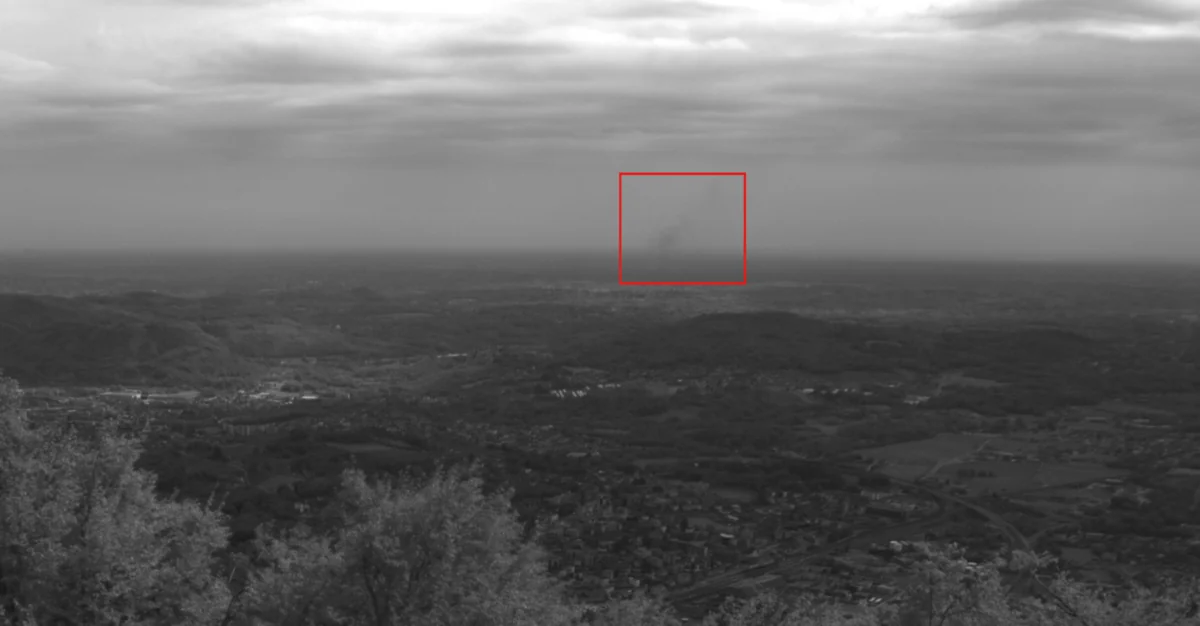 Immagine in scala di grigi della telecamera HUVI.NOMAD sulla pianura vicino a Milano, evidenziata in rosso la colonna di fumo rilevata a circa 17 km